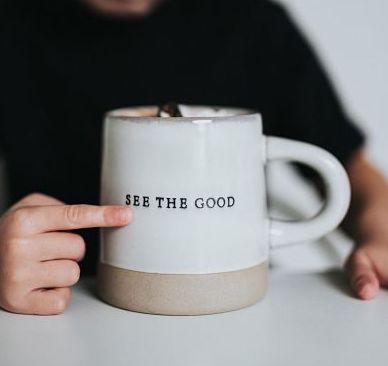 White coffee cup with finger pointing to "See the Good" on it